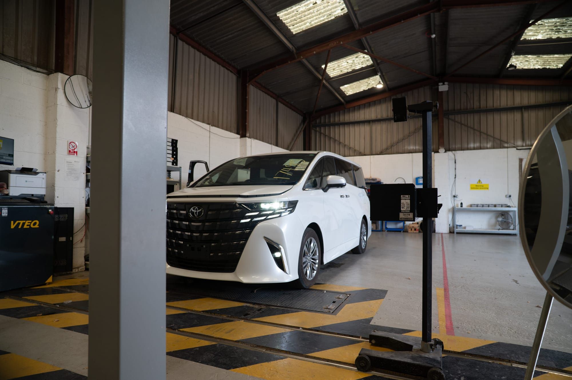 A white Toyota Alphard on the yellow-hatched test lane inside My Car Import's workshop
