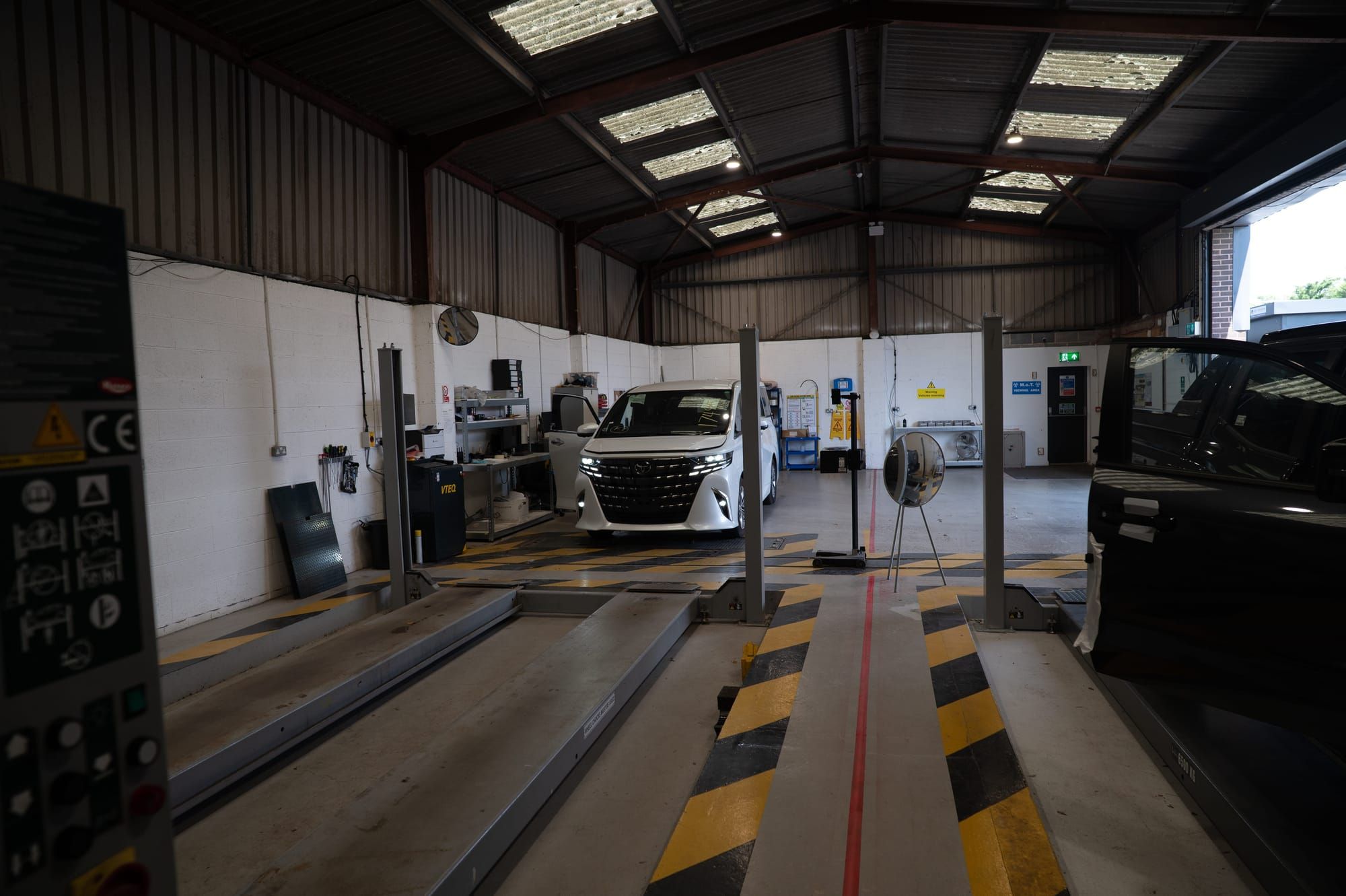 An Alphard between the lifts in My Car Import's workshop, with test lanes in the foreground